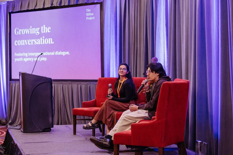 Marisol Jimenez and Jose Guallpa on stage in red armchairs beside a Rithm Project slide reading Growing the conversation.