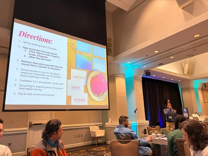 The AI Effect Workshop: a presenter speaks at the front of a ballroom beside a slide of directions for the opinion card activity.