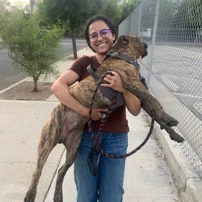 Marisol smiling while carrying her brindle dog in her arms.