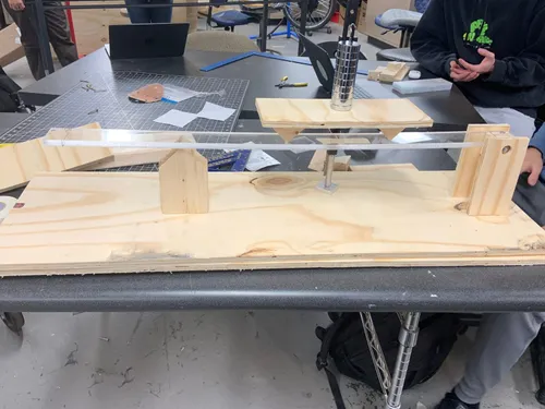 A wood and acrylic load-testing rig with a stack of steel weights, in an engineering shop.